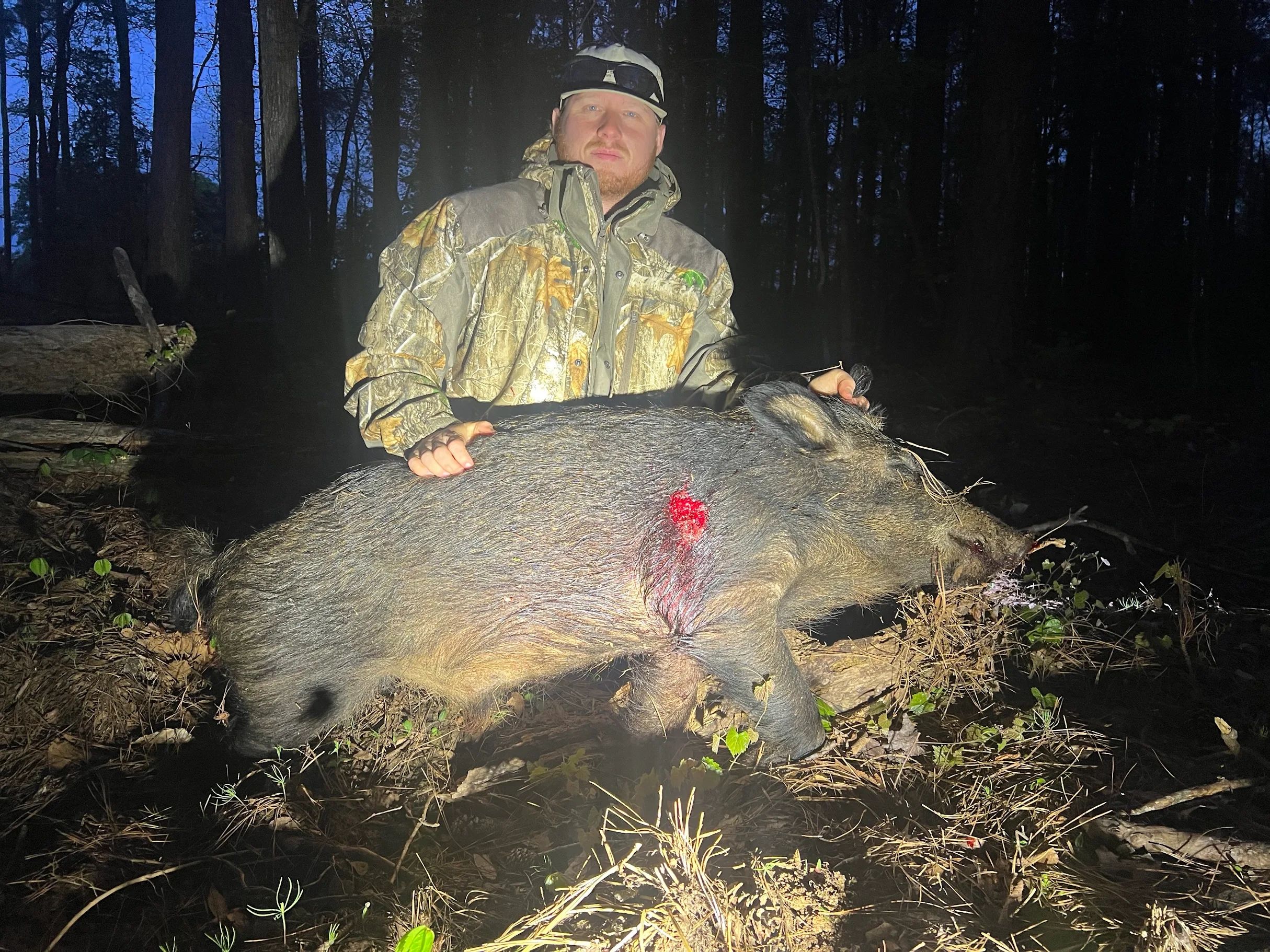 Man in camo jacket poses with large wild hog at night.
