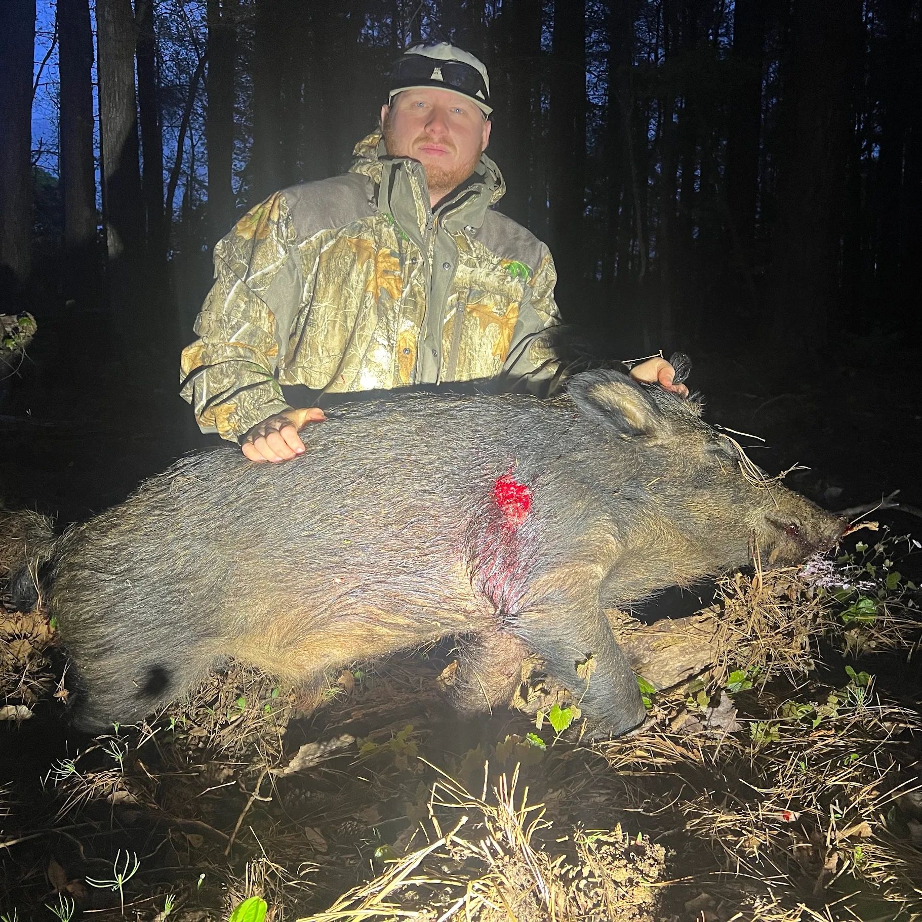 Hunter posing with a wild boar in a forest at night.