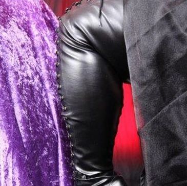 Close-up of a person wearing black leather pants with laces and a purple textured fabric background.