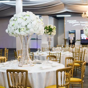Elegant banquet hall with floral centerpieces and gold chairs.