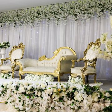 Elegant wedding stage with white flowers and golden chairs.