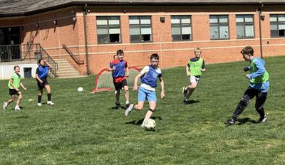 Kids playing soccer on a grassy field near a brick building.