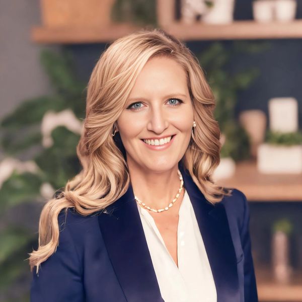 Professional woman with blonde hair smiling, wearing a navy blazer and white blouse.