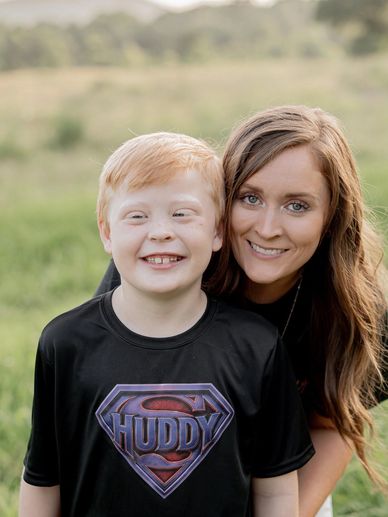 Smiling woman and boy outdoors in grassy field.