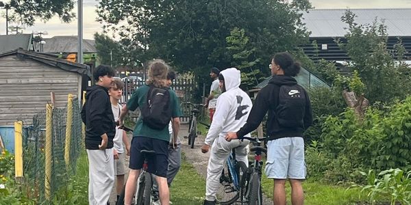 Group of young people with bikes chatting on a path near a garden.