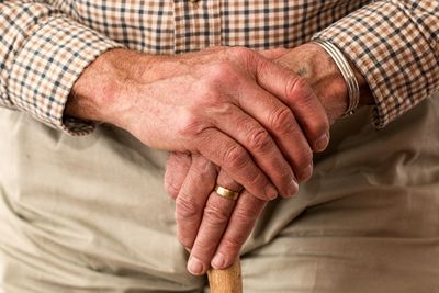 Elderly man's hands folded on top of cane.