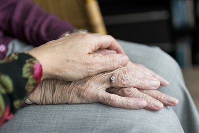 Person's hand on top of elderly person's hands, folded on lap.