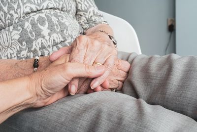 Person holding the hand of an elderly person, with hands folded on lap.