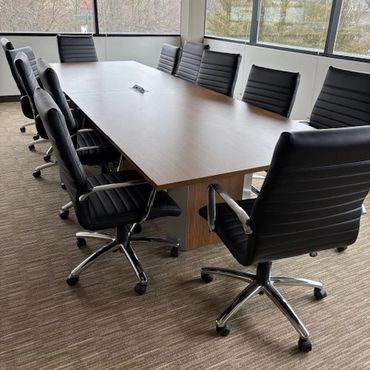 Empty boardroom with black chairs around a rectangular wooden table.