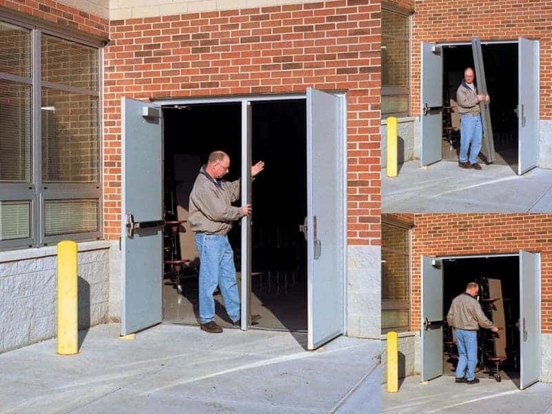A man demonstrates a collapsible door outside a brick building.