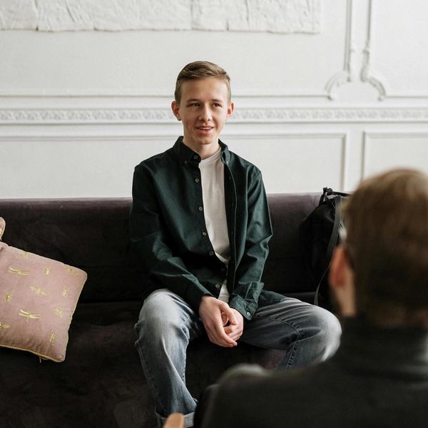 Teenage boy sitting on a couch, talking to a person in front of him.