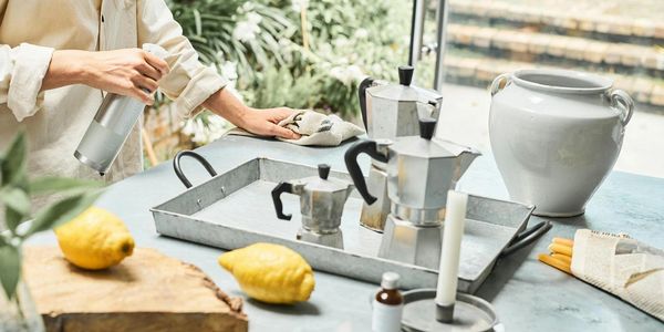 Person cleaning a table with coffee pots, lemons, and a ceramic vase on it.