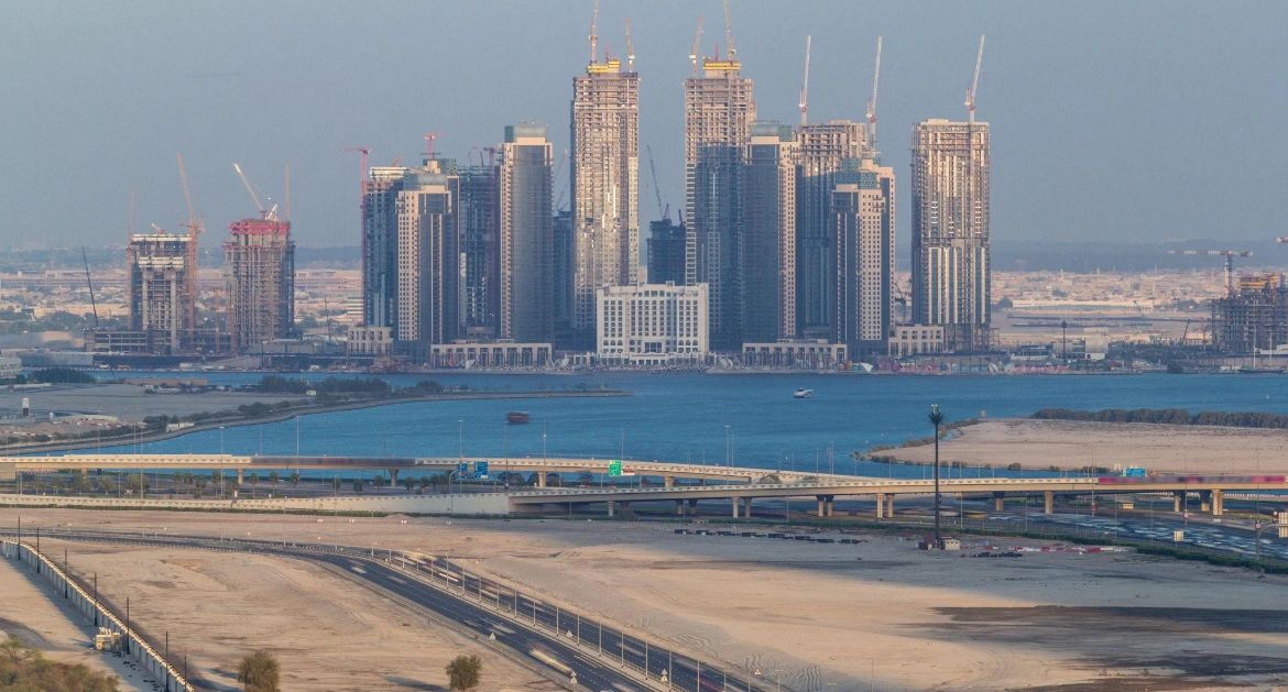 High-rise buildings under construction near a water body with highways in the foreground.