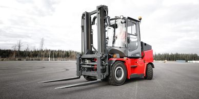 A red and black forklift on an empty paved area under a cloudy sky.