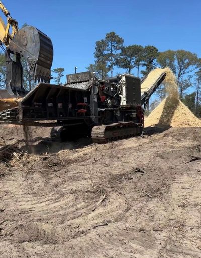 Heavy machinery processing wood chips outdoors under clear blue sky.