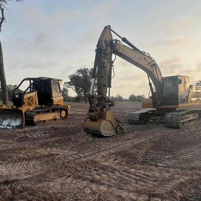 Two excavators parked on a dirt construction site at dawn.