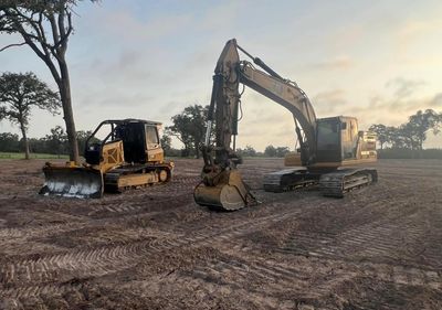 Two yellow excavators parked on a cleared dirt field during sunset.