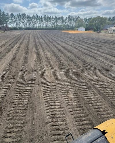 Freshly plowed field with tractor tracks under a cloudy sky.