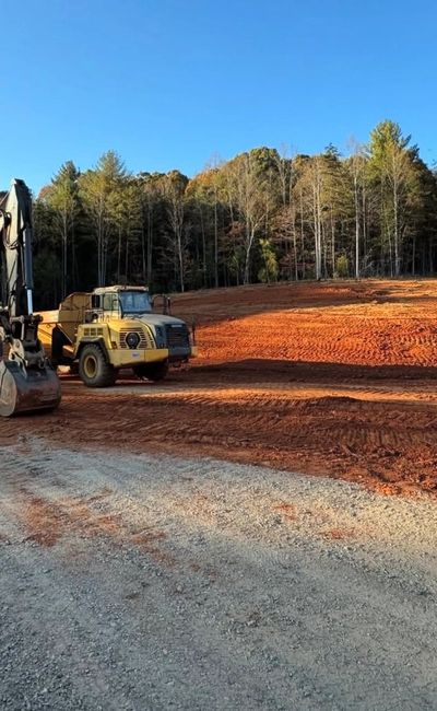 Construction vehicles on a cleared red soil site near a forest.
