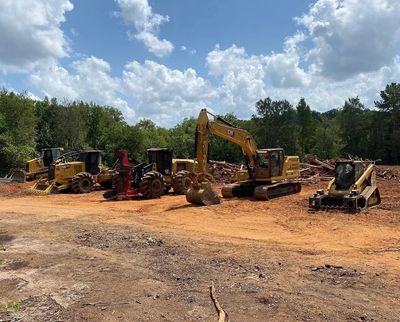 Construction machines lined up on a dirt clearing under a partly cloudy sky.