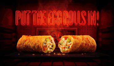 Crispy egg rolls with vibrant filling under a neon sign.