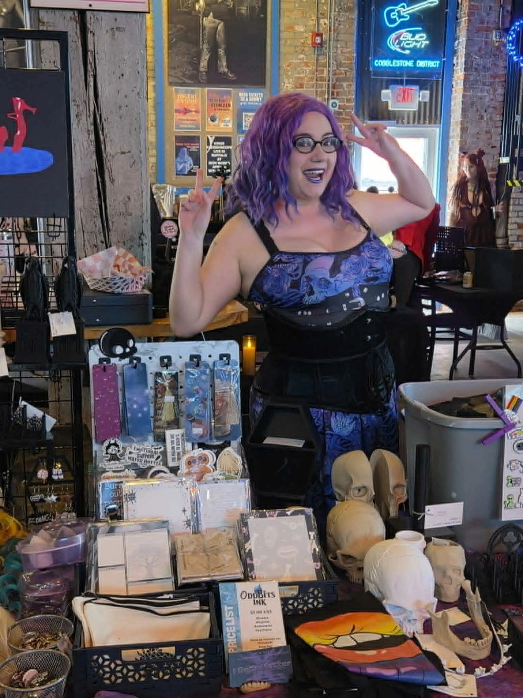 Woman with purple hair posing at a merchandise booth.