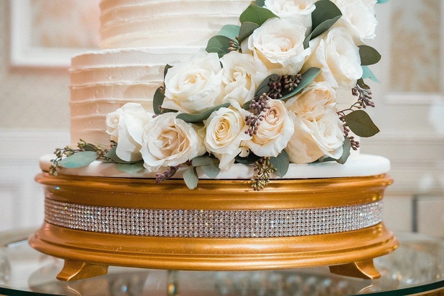 White frosting iced wedding cake with horizontal lines, sitting on top of a gold cake stand.