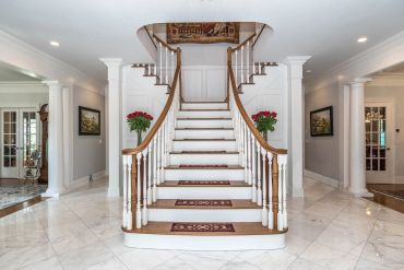 Elegant white staircase with wooden handrails in a bright foyer.