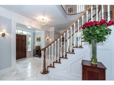 Elegant staircase with wooden banister and bouquet of red roses in a bright entrance hall.