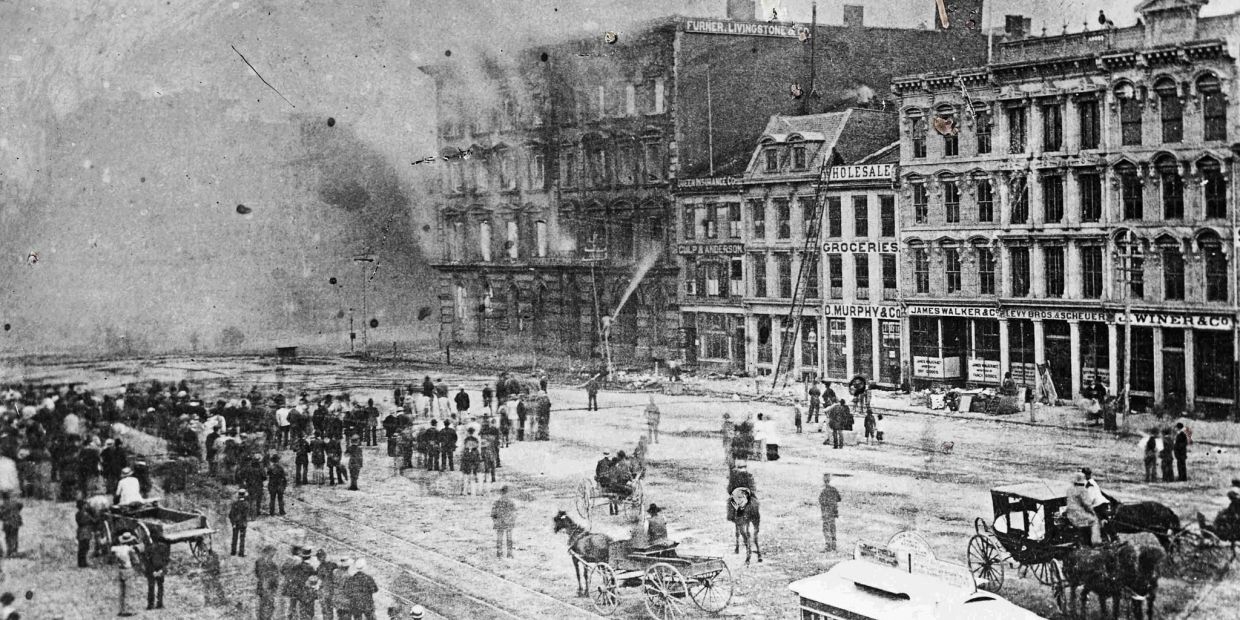 Crowd watching a building fire with early firefighting efforts.