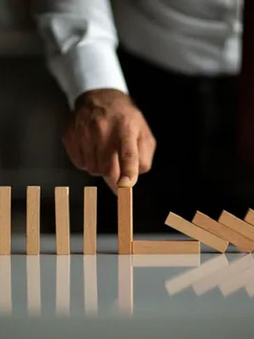 Hand stopping falling dominoes with a wooden block.