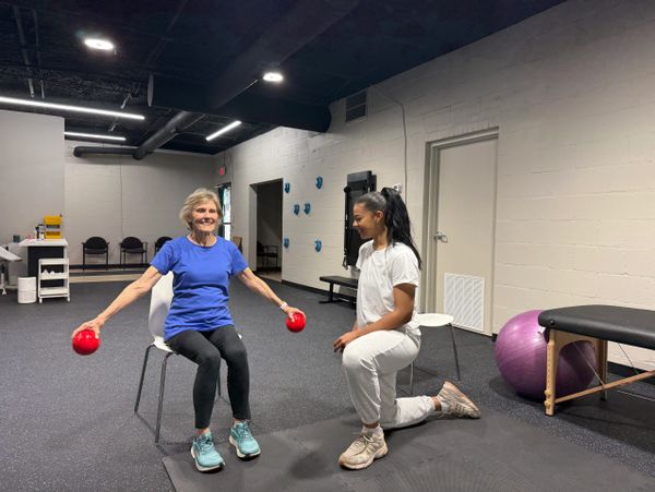 Older woman exercising with red weights while trainer guides her.