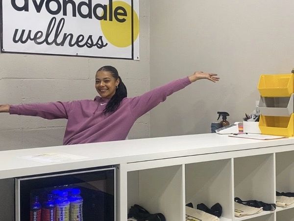 A woman in a purple sweatshirt smiles behind a wellness center counter.