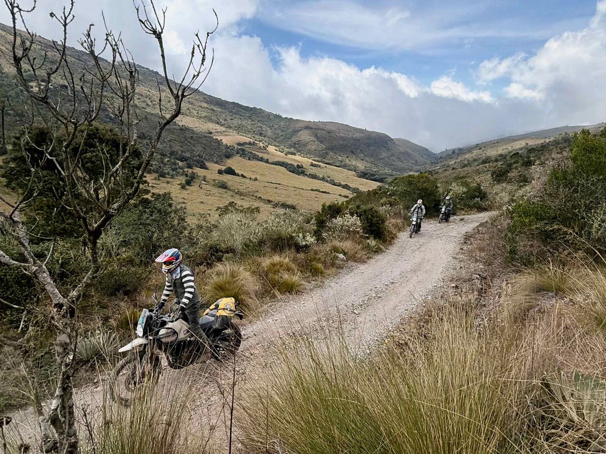 Three motorcyclists riding on a dirt road through a mountainous landscape.