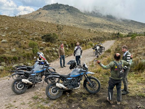 Four motorcyclists take a break on a mountain dirt road with their bikes.