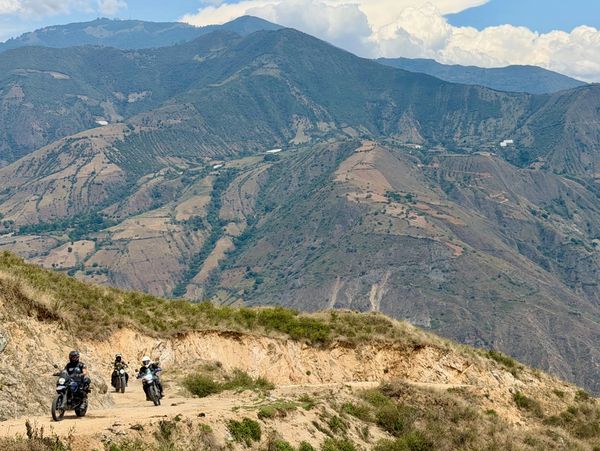Three motorcyclists ride on a rugged mountain dirt road.