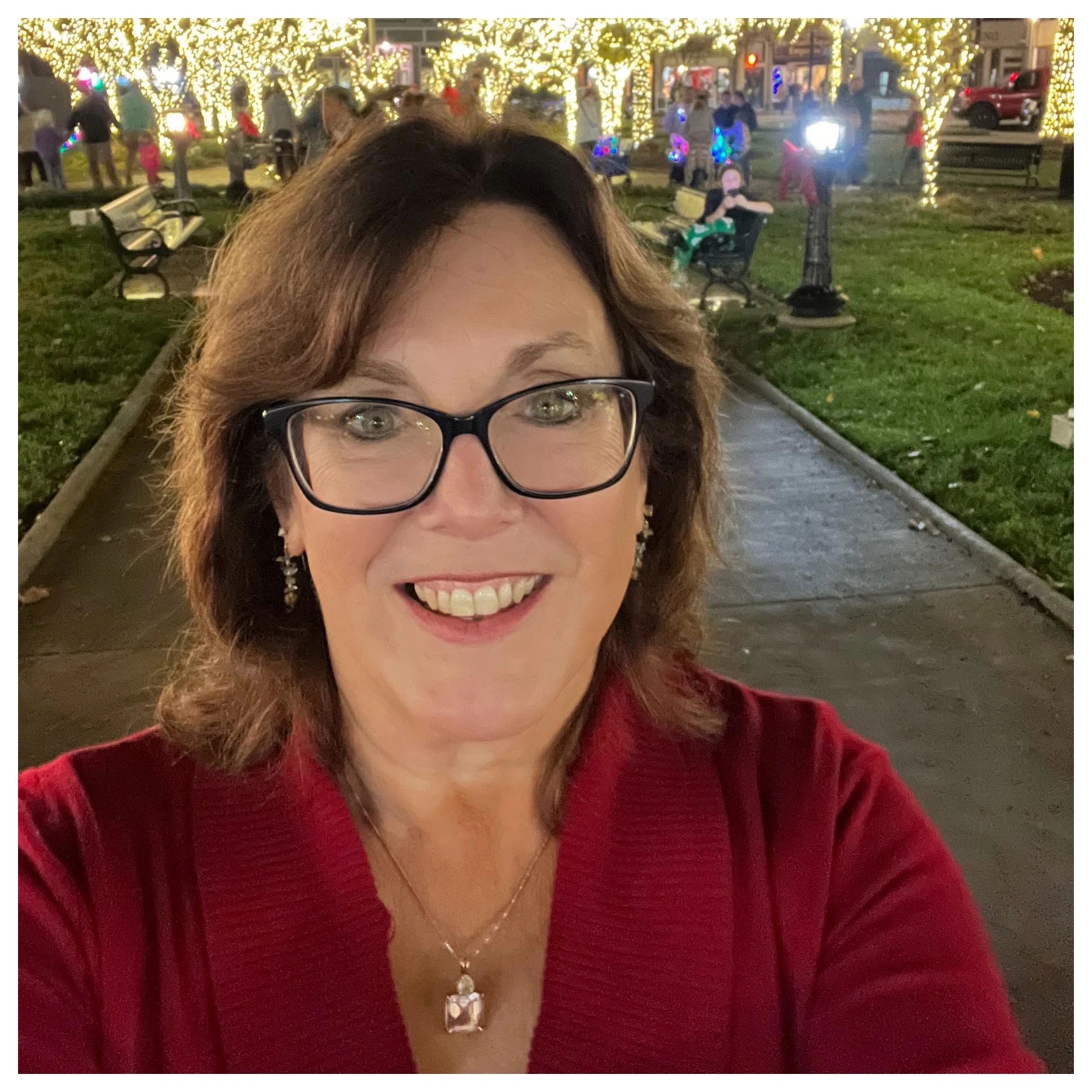 Margalena Walker smiling at the camera while taking a selfie in a festively lit park.