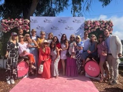 Group photo of people at an outdoor event with floral decorations and a pink carpet.