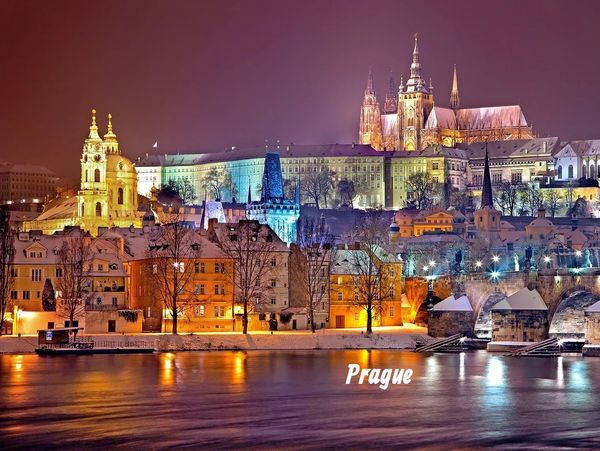 Night view of illuminated historic buildings in Prague by the river.