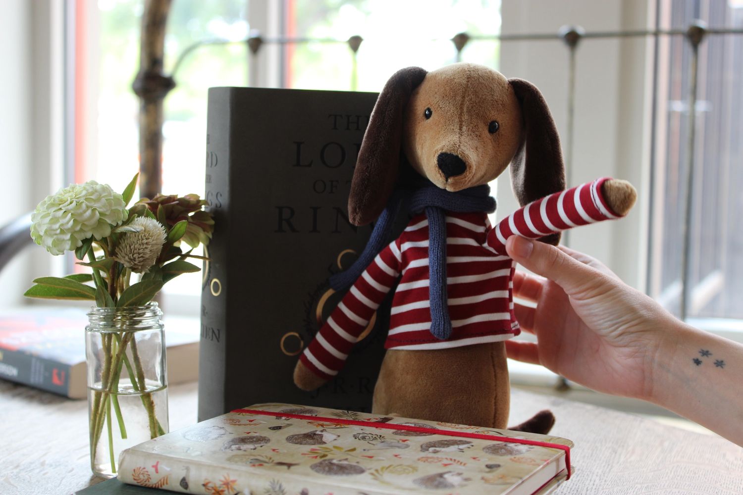 Toy dog waving in front of stack of notebooks, a small flower vase, and a grey book in the back.