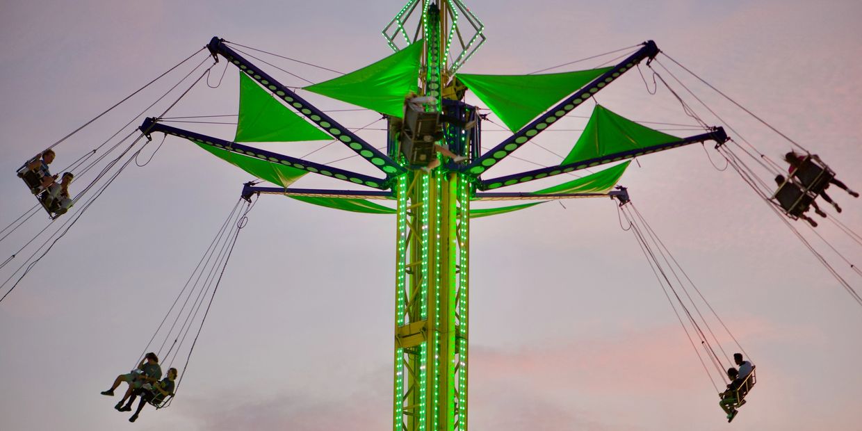 People riding a green-lit swing ride at dusk.