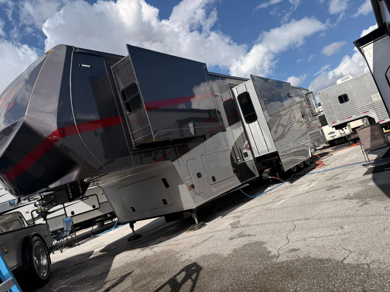 Large RV with extended slide-outs under a partly cloudy sky.