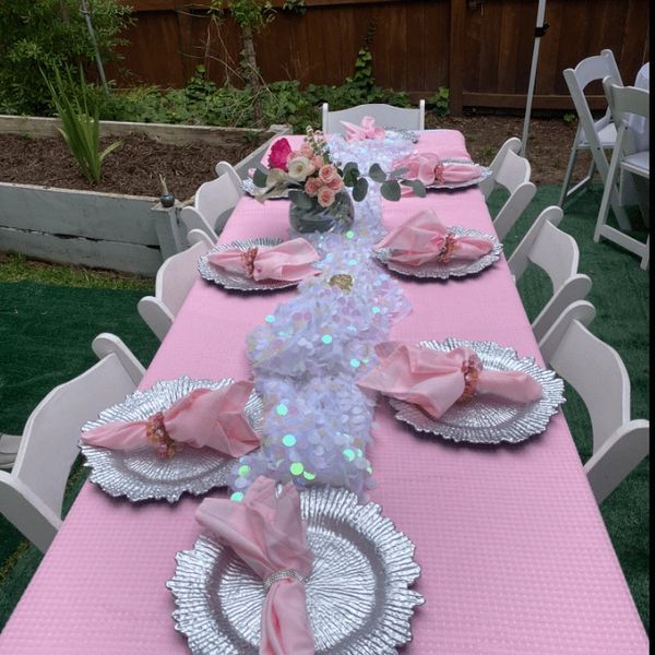 LACE Events luxurious, pink table setting with white folding chairs, silver plate coasters, & flower