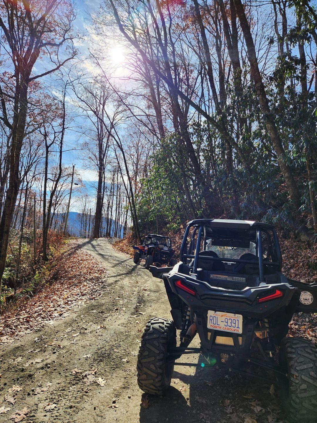 Two off-road vehicles on a sunny forest trail with autumn leaves.