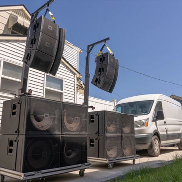 Large outdoor speaker setup with white van in background.