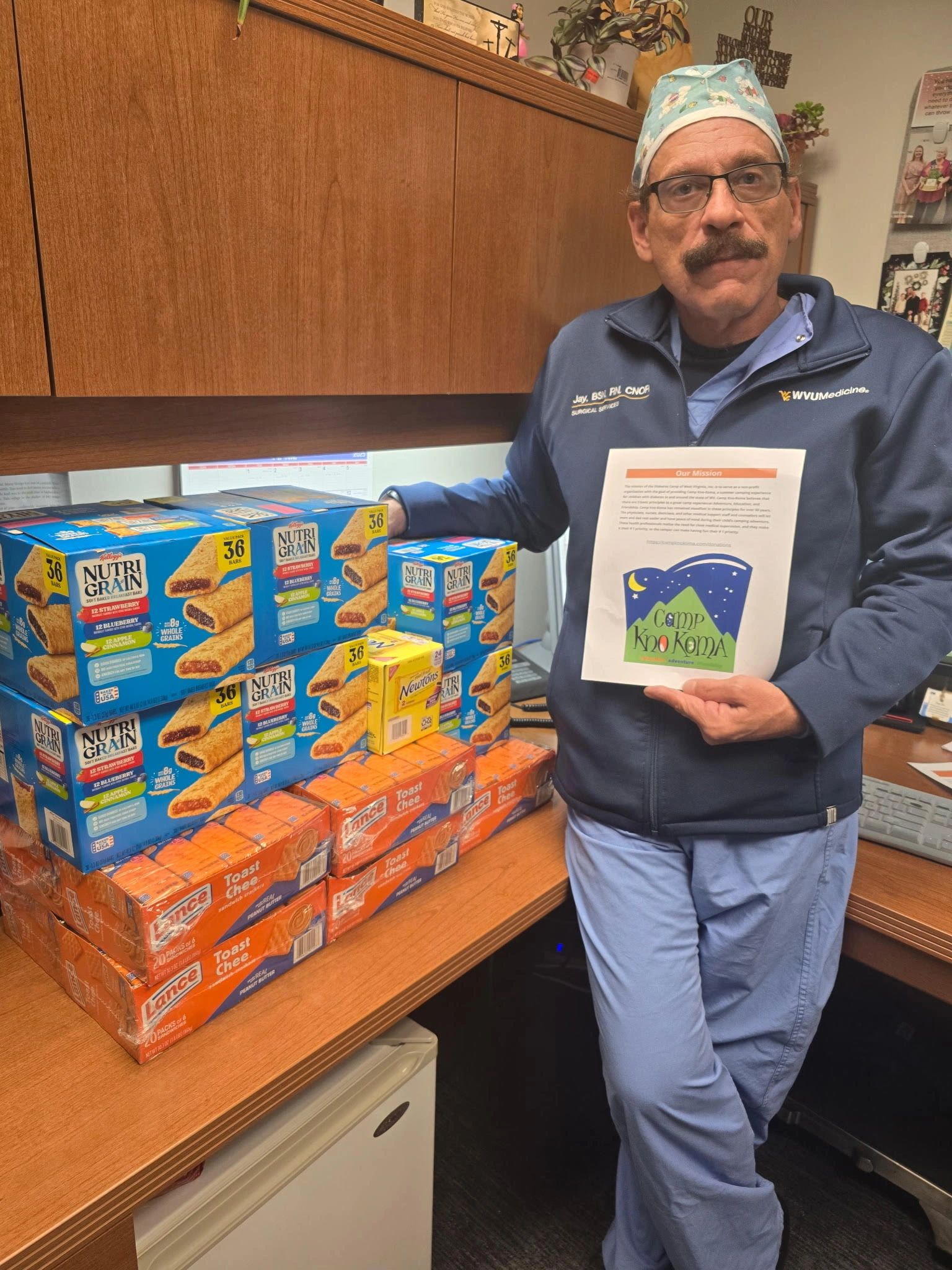 Man in scrubs holding a Camp Kno Koma flyer next to snacks.
