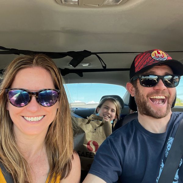 Selfie of a Mom, Dad, and child grinning while driving down the highway in Hawaii.
