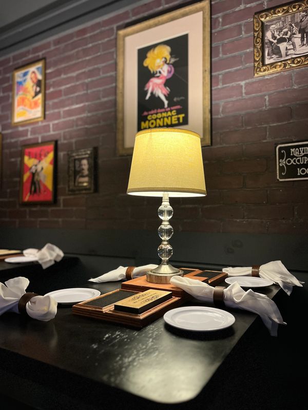 Cozy restaurant table set with plates, napkins, and a glowing lamp.