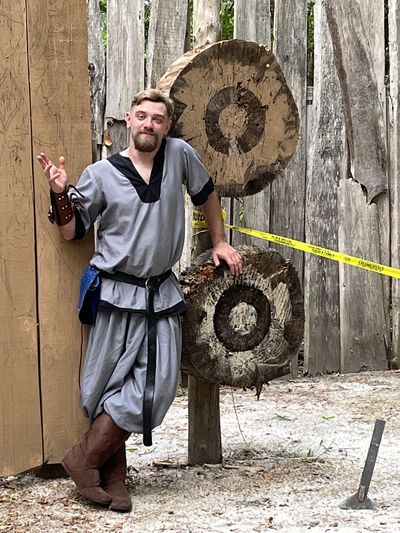 Man leaning on wooden target boards at an outdoor practice area.