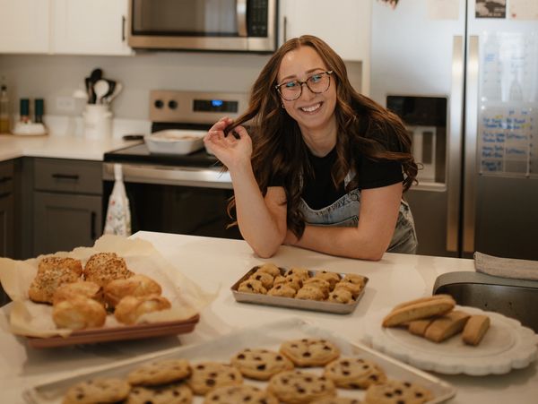 Smiling woman in kitchen with freshly baked cookies and bread.